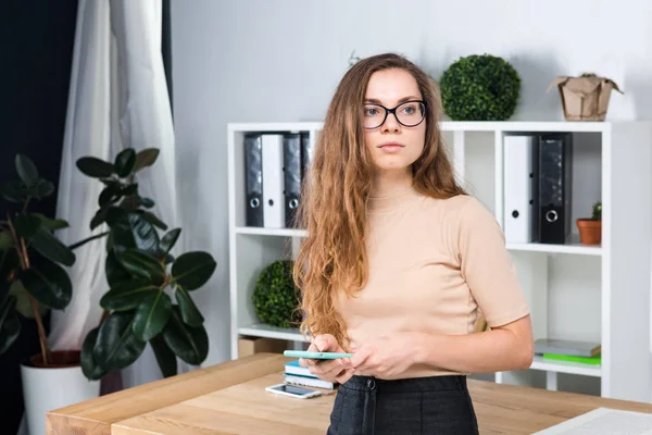 長い髪と摩擦のメガネの若い白人女性の肖像画は オフィス机近くオフィス部屋の中で立っています 大学生の女の子 学習トピックの男 — ストック写真
