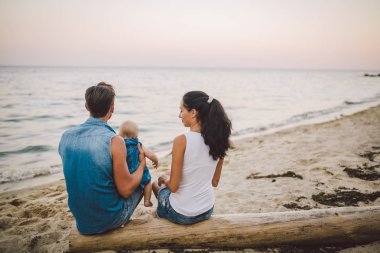 Tema Aile hafta sonu, plaj yaz tatili çocuk ile. Üç baba anne ve kızı genç şık aile yalancı ağaç sırtlarını ile bir yıl oturup, yaz aylarında bakan ufuk deniz günbatımı oturum.