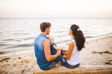 Tema Aile hafta sonu, plaj yaz tatili çocuk ile. Üç baba anne ve kızı genç şık aile yalancı ağaç sırtlarını ile bir yıl oturup, yaz aylarında bakan ufuk deniz günbatımı oturum.