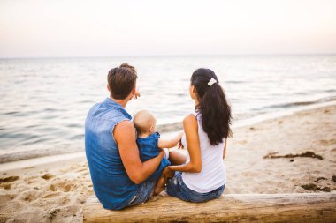 Tema Aile hafta sonu, plaj yaz tatili çocuk ile. Üç baba anne ve kızı genç şık aile yalancı ağaç sırtlarını ile bir yıl oturup, yaz aylarında bakan ufuk deniz günbatımı oturum.