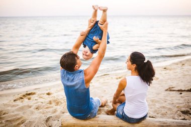 Tema Aile hafta sonu, plaj yaz tatili çocuk ile. Üç baba anne ve kızı genç şık aile yalancı ağaç sırtlarını ile bir yıl oturup, yaz aylarında bakan ufuk deniz günbatımı oturum.