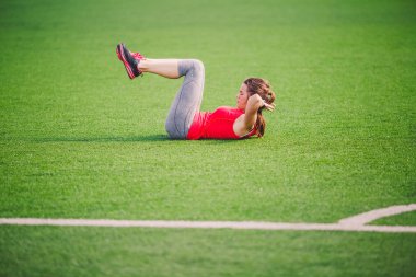 Tema spor ve sağlık. Isınma kadar kasları, karın kasları egzersiz, kaybeden göbek, karın yeşil çim Stadı yapay çim yaz aylarında ısınma, genç güzel beyaz kadının yapması