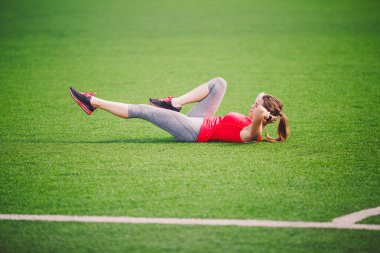 Tema spor ve sağlık. Isınma kadar kasları, karın kasları egzersiz, kaybeden göbek, karın yeşil çim Stadı yapay çim yaz aylarında ısınma, genç güzel beyaz kadının yapması