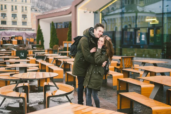 Ett ungt par i kärlek och en flicka och en student stå embracing nära tabellerna i en gatuterrass café vinterstängt tom utan människor. Lågsäsong catering restaurang dåligt väder — Stockfoto