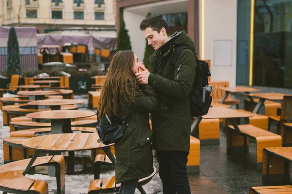 Młoda para w miłości i dziewczyna i stand student, obejmując w pobliżu tabel, z kawiarni na tarasie przy ulicy ZAMKNIĘTA pusty bez ludzi na zimę. Poza sezonem catering restauracja złej pogody — Zdjęcie stockowe