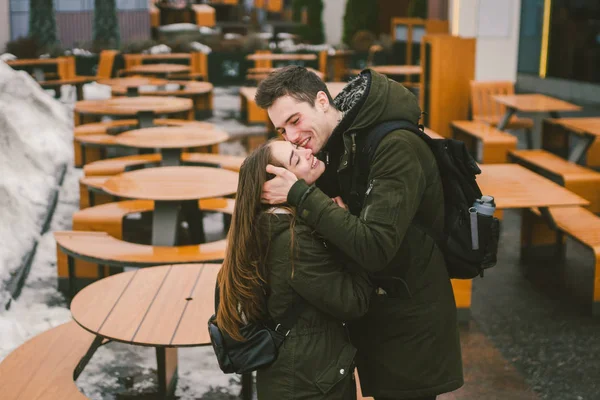 Una joven pareja enamorada y una niña y un estudiante de pie abrazando cerca de las mesas de una terraza cafetería calle cerrada vacía sin gente para el invierno. Restaurante de catering fuera de temporada mal tiempo —  Fotos de Stock