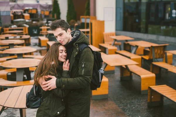 一对恋爱中的年轻夫妇和一个女孩和一个学生站在一个街道露台咖啡馆的桌子旁拥抱 空无一人 没有人过冬 淡季餐饮餐厅恶劣天气 — 图库照片