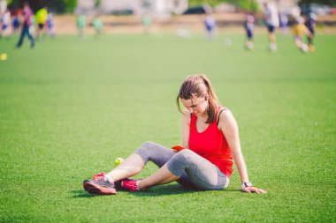 Tema spor sağlık. güzel genç kız oturan yeşil çimenlerin üzerinde dinlenme. çim Stadı technodogies kullanarak. Handphone kulak kulaklık müzik, yaz spor giyim akıllı seyretmek kalp oran sınıf başkanı dinler