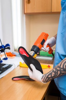 portre dövme atölye mavi üniforma giymiş olan genç adam elinde bireysel ortopedik tabanlık olun. Araç ısı ve deforme için saç kurutma makinesi kullanır. Küçük işletme ve tıp Tema.