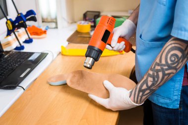 portre dövme atölye mavi üniforma giymiş olan genç adam elinde bireysel ortopedik tabanlık olun. Araç ısı ve deforme için saç kurutma makinesi kullanır. Küçük işletme ve tıp Tema.