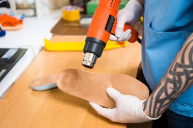 portre dövme atölye mavi üniforma giymiş olan genç adam elinde bireysel ortopedik tabanlık olun. Araç ısı ve deforme için saç kurutma makinesi kullanır. Küçük işletme ve tıp Tema.