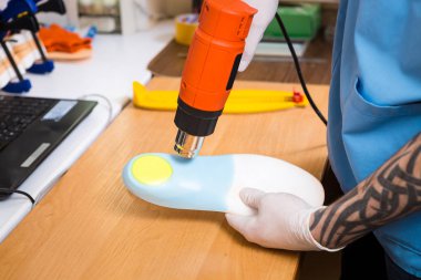 portre dövme atölye mavi üniforma giymiş olan genç adam elinde bireysel ortopedik tabanlık olun. Araç ısı ve deforme için saç kurutma makinesi kullanır. Küçük işletme ve tıp Tema.