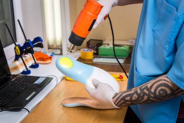 portre dövme atölye mavi üniforma giymiş olan genç adam elinde bireysel ortopedik tabanlık olun. Araç ısı ve deforme için saç kurutma makinesi kullanır. Küçük işletme ve tıp Tema.
