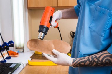 portre dövme atölye mavi üniforma giymiş olan genç adam elinde bireysel ortopedik tabanlık olun. Araç ısı ve deforme için saç kurutma makinesi kullanır. Küçük işletme ve tıp Tema.