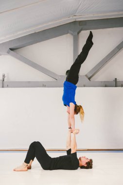 Spor ve dönüm temasıdır. Paspaslar üzerinde beyaz bir spor salonunda akrobatik yoga uygulamak genç bir beyaz erkek ve kadın çift. bir adam sırt üstü yatıyor ve bir kadın genişletilmiş silah tutar. El poz