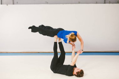 Spor ve dönüm temasıdır. Paspaslar üzerinde beyaz bir spor salonunda akrobatik yoga uygulamak genç bir beyaz erkek ve kadın çift. bir adam sırt üstü yatıyor ve bir kadın genişletilmiş silah tutar. El poz