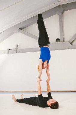 Spor ve dönüm temasıdır. Paspaslar üzerinde beyaz bir spor salonunda akrobatik yoga uygulamak genç bir beyaz erkek ve kadın çift. bir adam sırt üstü yatıyor ve bir kadın genişletilmiş silah tutar. El poz.