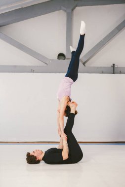 Spor ve dönüm temasıdır. Paspaslar üzerinde beyaz bir spor salonunda akrobatik yoga uygulamak genç bir beyaz erkek ve kadın çift. bir adam sırt üstü yatıyor ve bir kadın genişletilmiş silah tutar. El poz