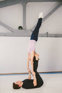 Spor ve dönüm temasıdır. Paspaslar üzerinde beyaz bir spor salonunda akrobatik yoga uygulamak genç bir beyaz erkek ve kadın çift. bir adam sırt üstü yatıyor ve bir kadın genişletilmiş silah tutar. El poz