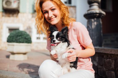 İnsan ve hayvan dostluk temasıdır. Yaz aylarında güneşli havalarda bina bir ev yakınındaki bir evcil köpek Chihuahua cins tutan güzel genç Kızıl saçlı beyaz kadın.