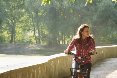 Konu ekolojik bisiklet taşıma. Beyaz genç bir kadın bir toprak yola yakın bir göl güneşli havalarda sonbaharda bir turuncu renkli Bisiklet Kiralama bir parkta sürme.
