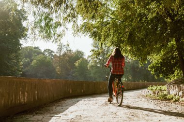 Konu ekolojik bisiklet taşıma. Beyaz genç bir kadın bir toprak yola yakın bir göl güneşli havalarda sonbaharda bir turuncu renkli Bisiklet Kiralama bir parkta sürme.