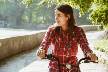 Konu ekolojik bisiklet taşıma. Güneşli havalarda sonbaharda bir dinlenme için poz bir turuncu renkli Bisiklet Kiralama bir Gölü yakınındaki bir parkta bir toprak yol üzerinde genç beyaz kadın.