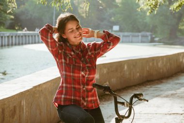 Konu ekolojik bisiklet taşıma. Güneşli havalarda sonbaharda bir dinlenme için poz bir turuncu renkli Bisiklet Kiralama bir Gölü yakınındaki bir parkta bir toprak yol üzerinde genç beyaz kadın.