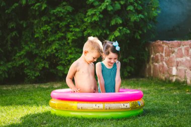 Tema bir çocuk Yaz tatilindeyiz. İki beyaz çocuk, kardeşi ve kız kardeşi, suyla bir mayo ve sevinç mutluluk gülümseme yeşil çim bahçesinde tünemiş bir yuvarlak havuzda oturup.