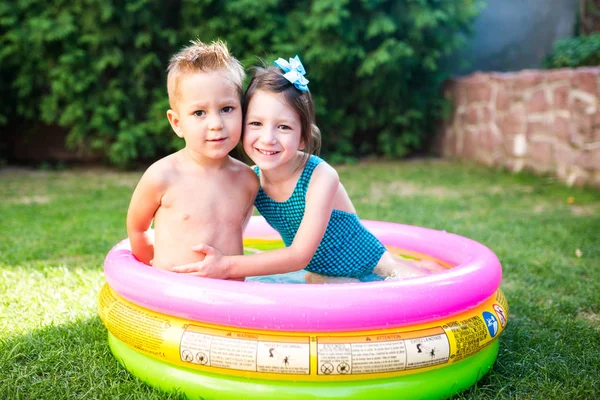 テーマは 子供の夏休みです 白人のお子様が 兄と妹 水着と喜び幸せ笑顔で緑の芝生の庭に水宙は円形プールで座る — ストック写真