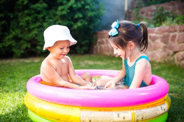 テーマは 子供の夏休みです 白人のお子様が 兄と妹 水着と喜び幸せ笑顔で緑の芝生の庭に水宙は円形プールで座る — ストック写真