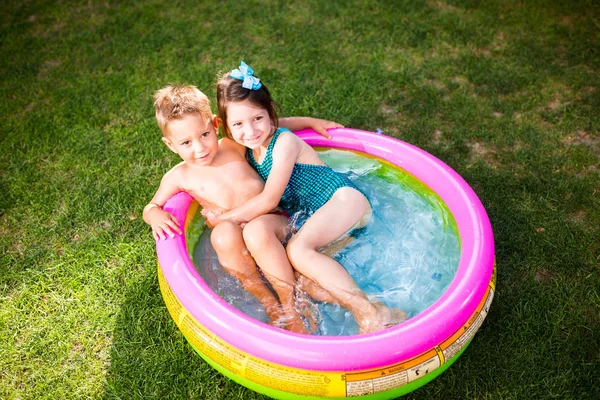 テーマは 子供の夏休みです 白人のお子様が 兄と妹 水着と喜び幸せ笑顔で緑の芝生の庭に水宙は円形プールで座る — ストック写真