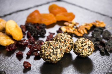 Tema şekerli tatlı şeker olmadan doğal ürünlerden yapılmış. Çöller Ball makro yakın çekim yuvarlak şeker truffle doğal kurutulmuş meyve ve beyaz ve siyah susam ve keten tohumu ile siyah bir plaka üzerinde.