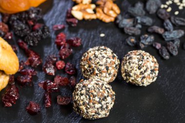 Tema şekerli tatlı şeker olmadan doğal ürünlerden yapılmış. Çöller Ball makro yakın çekim yuvarlak şeker truffle doğal kurutulmuş meyve ve beyaz ve siyah susam ve keten tohumu ile siyah bir plaka üzerinde.