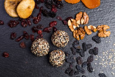 Tema şekerli tatlı şeker olmadan doğal ürünlerden yapılmış. Çöller Ball makro yakın çekim yuvarlak şeker truffle doğal kurutulmuş meyve ve beyaz ve siyah susam ve keten tohumu ile siyah bir plaka üzerinde.
