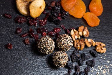 Tema şekerli tatlı şeker olmadan doğal ürünlerden yapılmış. Çöller Ball makro yakın çekim yuvarlak şeker truffle doğal kurutulmuş meyve ve beyaz ve siyah susam ve keten tohumu ile siyah bir plaka üzerinde.