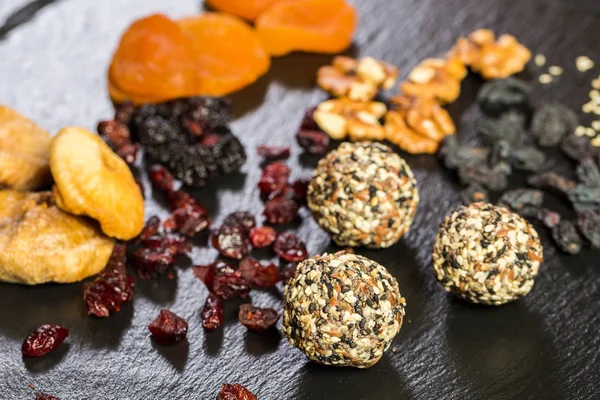 Theme sweet dessert made from natural products without sugar. Macro close-up of deserts ball round candy truffle on a black plate with natural dried fruit and seeds of white and black sesame and flax.