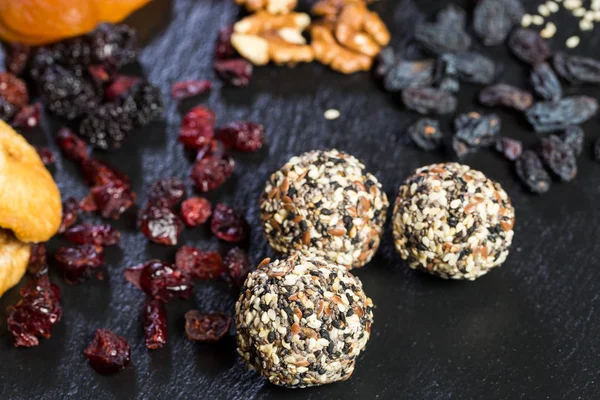 Theme sweet dessert made from natural products without sugar. Macro close-up of deserts ball round candy truffle on a black plate with natural dried fruit and seeds of white and black sesame and flax.