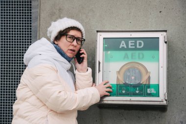 Tıp Kardiyopulmoner resüsitasyon acil çağrı yapıyorum. Kafkas kadın 911 yardım aramakta telefon kullanır. Cihaz kutusu aed otomatik defibrilatör hastalıkları, klinik ölüm, kalp durması ve kalp krizi