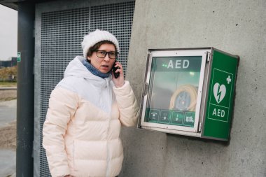 Tıp Kardiyopulmoner resüsitasyon acil çağrı yapıyorum. Kafkas kadın 911 yardım aramakta telefon kullanır. Cihaz kutusu aed otomatik defibrilatör hastalıkları, klinik ölüm, kalp durması ve kalp krizi