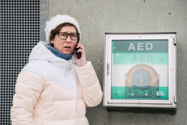 Tıp Kardiyopulmoner resüsitasyon acil çağrı yapıyorum. Kafkas kadın 911 yardım aramakta telefon kullanır. Cihaz kutusu aed otomatik defibrilatör hastalıkları, klinik ölüm, kalp durması ve kalp krizi