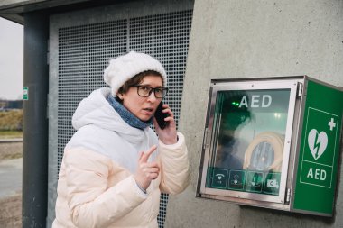 Tıp Kardiyopulmoner resüsitasyon acil çağrı yapıyorum. Kafkas kadın 911 yardım aramakta telefon kullanır. Cihaz kutusu aed otomatik defibrilatör hastalıkları, klinik ölüm, kalp durması ve kalp krizi