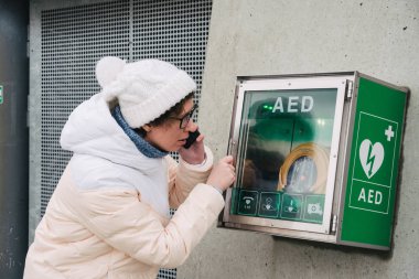 Tıp Kardiyopulmoner resüsitasyon acil çağrı yapıyorum. Kafkas kadın 911 yardım aramakta telefon kullanır. Cihaz kutusu aed otomatik defibrilatör hastalıkları, klinik ölüm, kalp durması ve kalp krizi