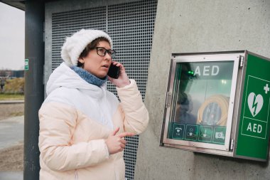 Tıp Kardiyopulmoner resüsitasyon acil çağrı yapıyorum. Kafkas kadın 911 yardım aramakta telefon kullanır. Cihaz kutusu aed otomatik defibrilatör hastalıkları, klinik ölüm, kalp durması ve kalp krizi