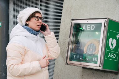 Tıp Kardiyopulmoner resüsitasyon acil çağrı yapıyorum. Kafkas kadın 911 yardım aramakta telefon kullanır. Cihaz kutusu aed otomatik defibrilatör hastalıkları, klinik ölüm, kalp durması ve kalp krizi