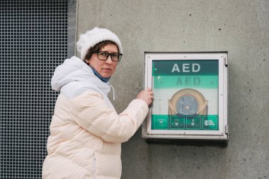 Tıp Kardiyopulmoner resüsitasyon ve acil arama. Genç Kafkas kadın yardım istiyor. Cihaz kutusu aed otomatik defibrilatör hastalıkları, klinik ölüm, kalp durması ve kalp krizi.