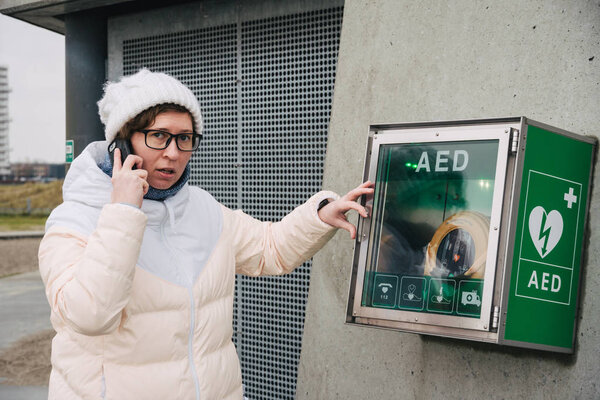 медицинская кардиолегочная реанимация срочный вызов. Белая женщина звонит 911 по телефону. устройство коробка aed автоматические дефибрилляторные заболевания, клиническая смерть, остановка сердца и сердечный приступ
