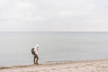 Bir beyaz adam genç Kafkas kadın turist kışın Baltık Denizi yakınında kumlu bir plaj üzerinde siyah bir sırt çantası ile. Tema yolculuk yalnız. Düşünce ve hayalleri ufuk bakan