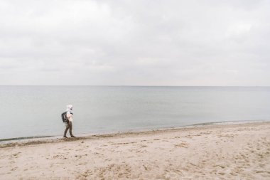 Bir beyaz adam genç Kafkas kadın turist kışın Baltık Denizi yakınında kumlu bir plaj üzerinde siyah bir sırt çantası ile. Tema yolculuk yalnız. Düşünce ve hayalleri ufuk bakan