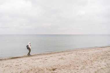 Bir beyaz adam genç Kafkas kadın turist kışın Baltık Denizi yakınında kumlu bir plaj üzerinde siyah bir sırt çantası ile. Tema yolculuk yalnız. Düşünce ve hayalleri ufuk bakan